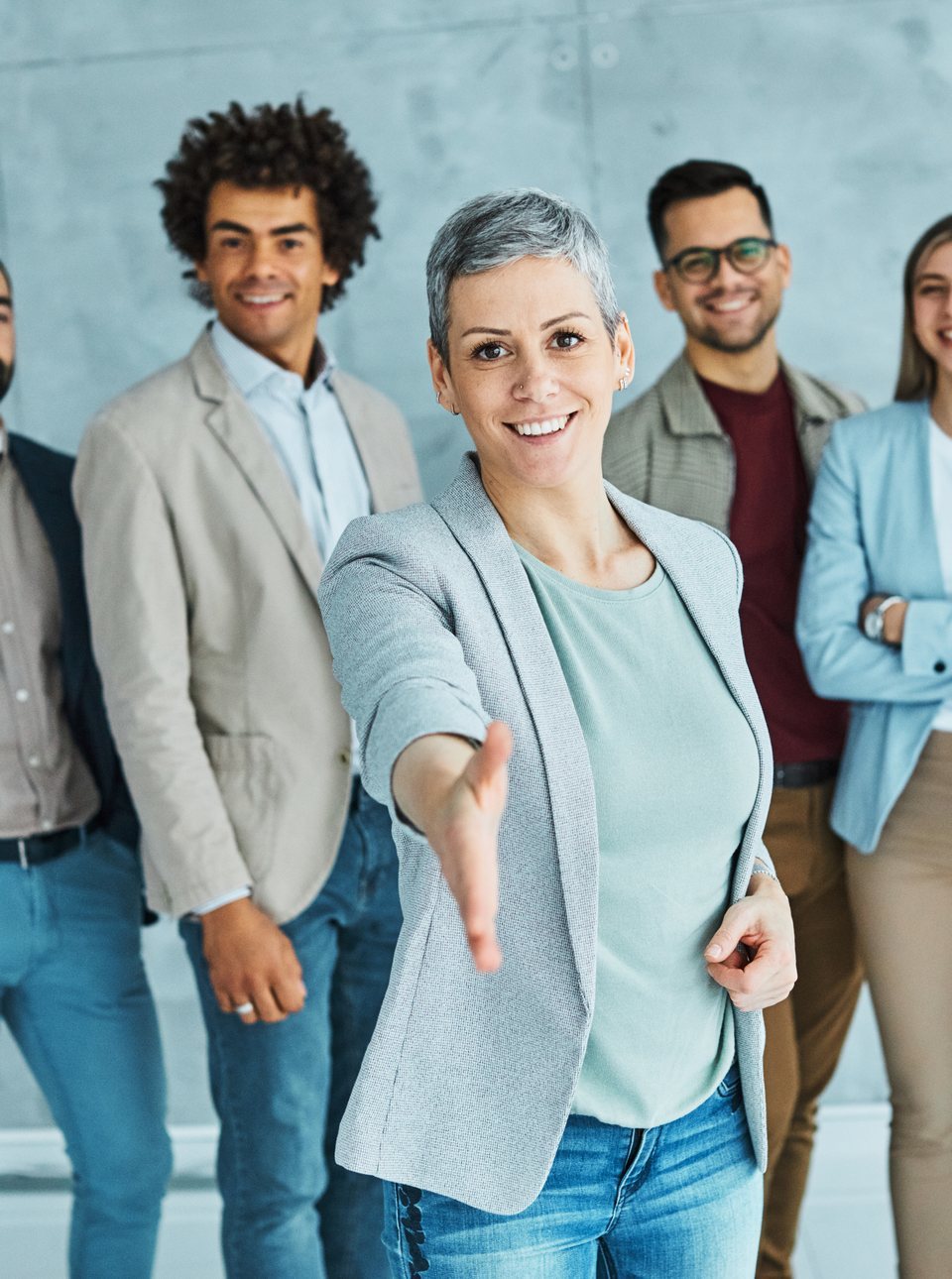 A smiling professional offering a handshake, with her team behind her