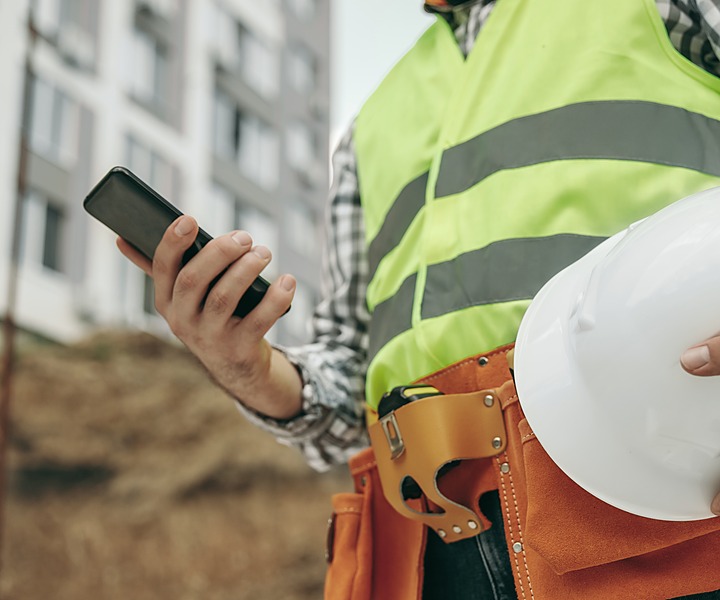 A construction worker in hi-vis checking his phone on site